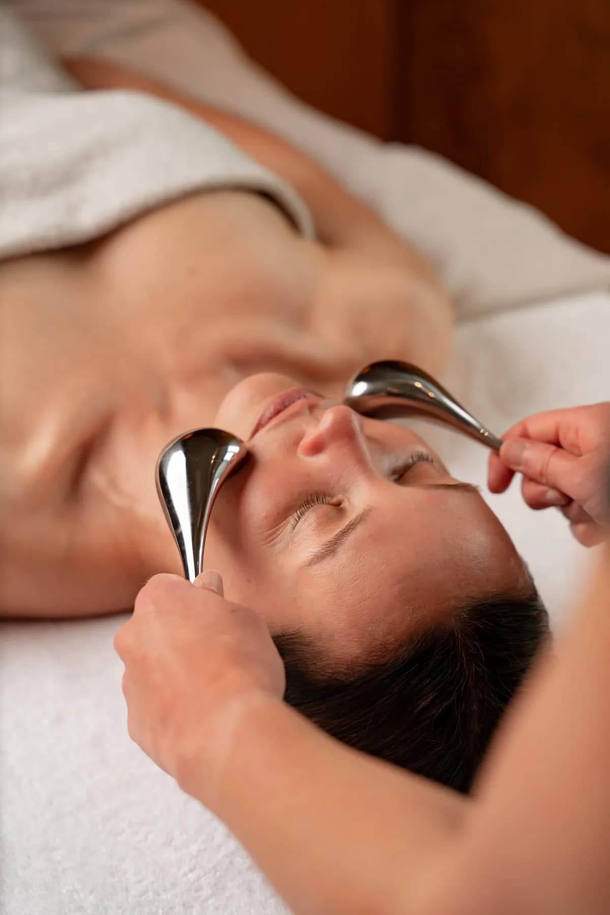 Soin du visage aux outils en inox prodigué à une cliente allongée dans un spa