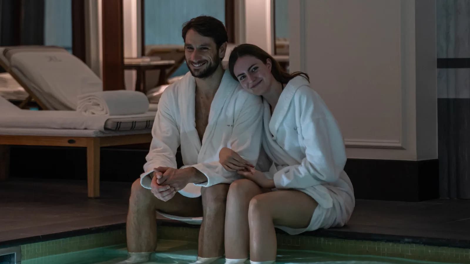 Offer treatment card Couple in bathrobes sitting by the pool of a Paris spa, feet in the water